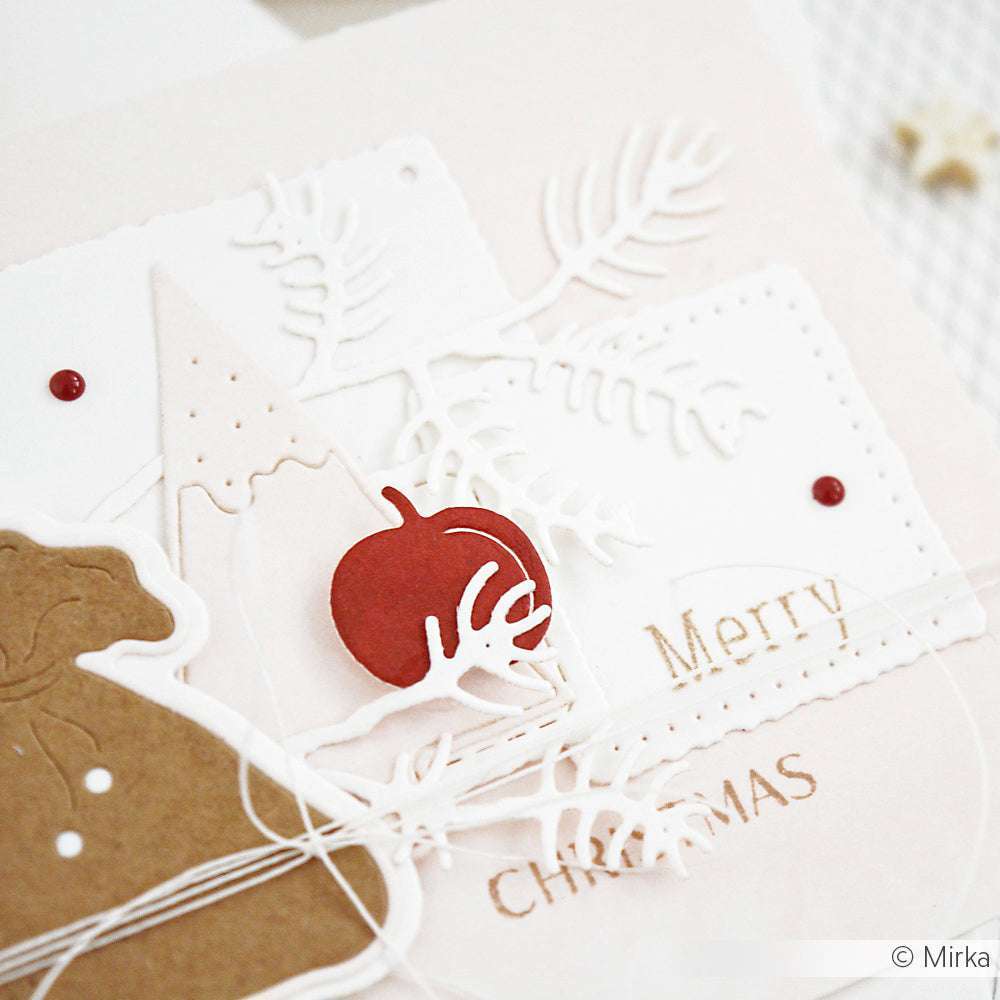 Nahaufnahme einer handgefertigten Weihnachtskarte mit "Frohe Weihnachten", einem roten Ornament, weißen Papierausschnitten und dekorativen Stanzformen von Alexandra Renke für festliches Flair.