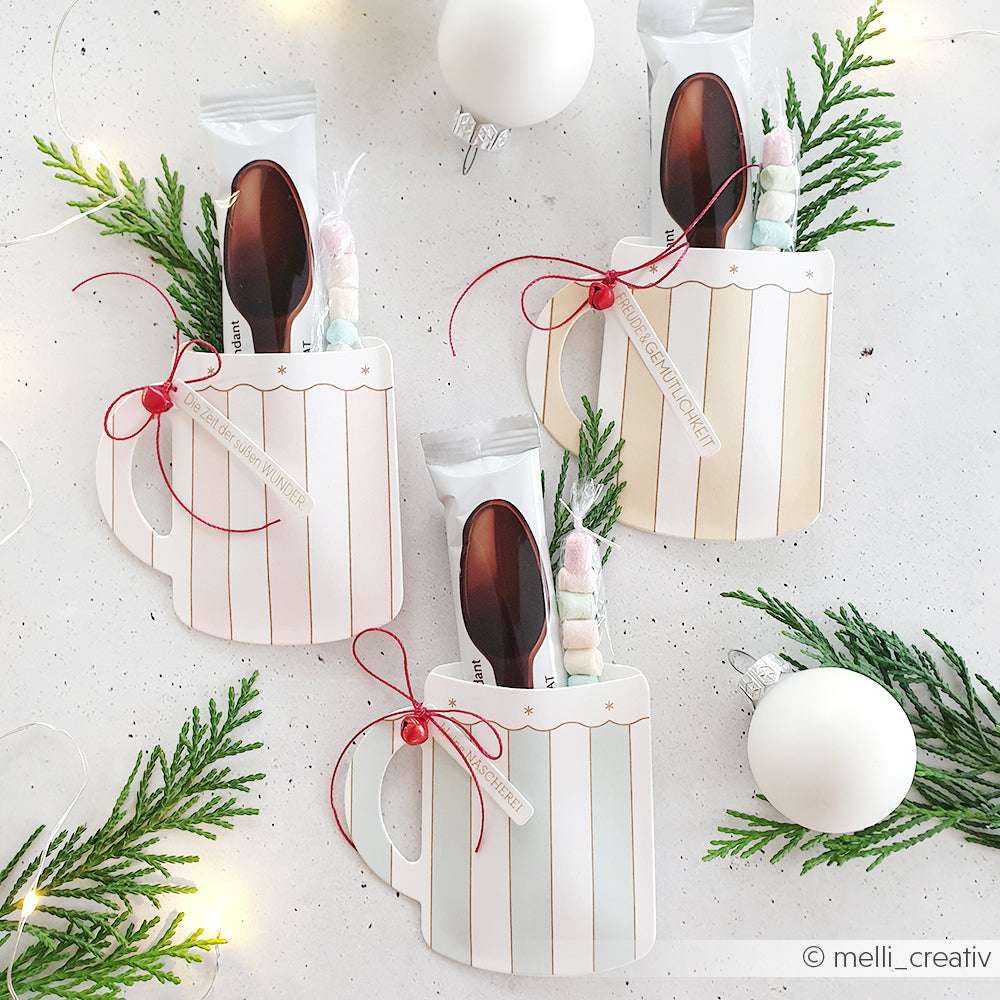 Ein Set aus drei becherförmigen Papiergeschenkbehältern von Alexandra Renke, hergestellt aus Designpapier und wunderschön dekoriert mit heißer Schokolade, Löffeln, Marshmallows, Grünzeug und Ornamenten - perfekt zum Verschenken und mit gestanzten Details verziert.