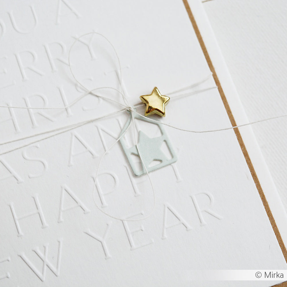 Weiße Prägekarte von Alexandra Renke mit einem goldenen Stern, einer dünnen Schnur und einem kleinen hausförmigen Ausschnitt, der mit komplizierten Dies-Details versehen ist.