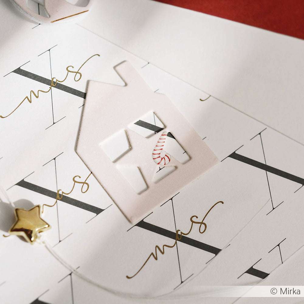 Ein weißes Papierhaus, das mit der Stanze Alexandra Renke Haus mit Stern-Rahmen ausgestanzt wurde, liegt auf einem weihnachtlichen Geschenkpapier, das mit einer goldenen Sternklammer und einem Band verziert ist.