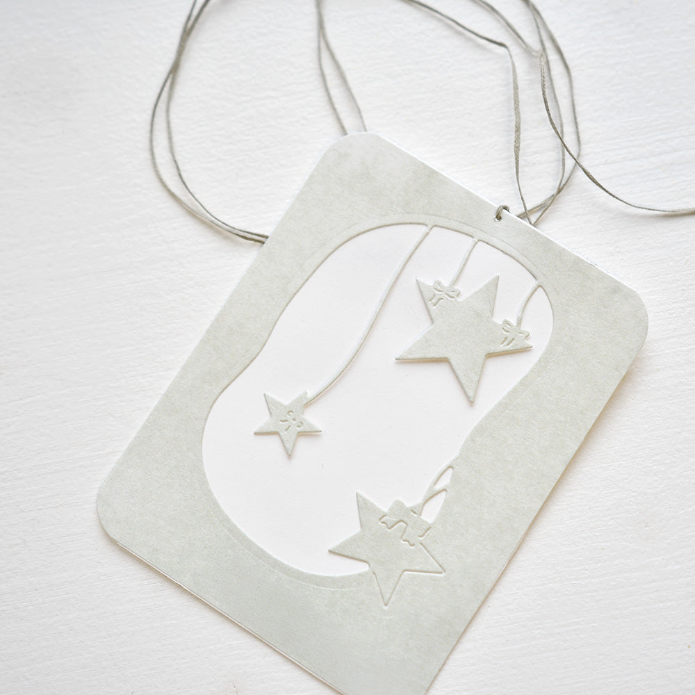 Eine weiße Karte mit ausgeschnittenen Sternen und einer Schnur, die mit dem Alexandra Renke Motivstanze Sternen Mobile hergestellt wurde, liegt auf einer weißen Fläche - ideal, um Ihren Designpapieren Eleganz zu verleihen.