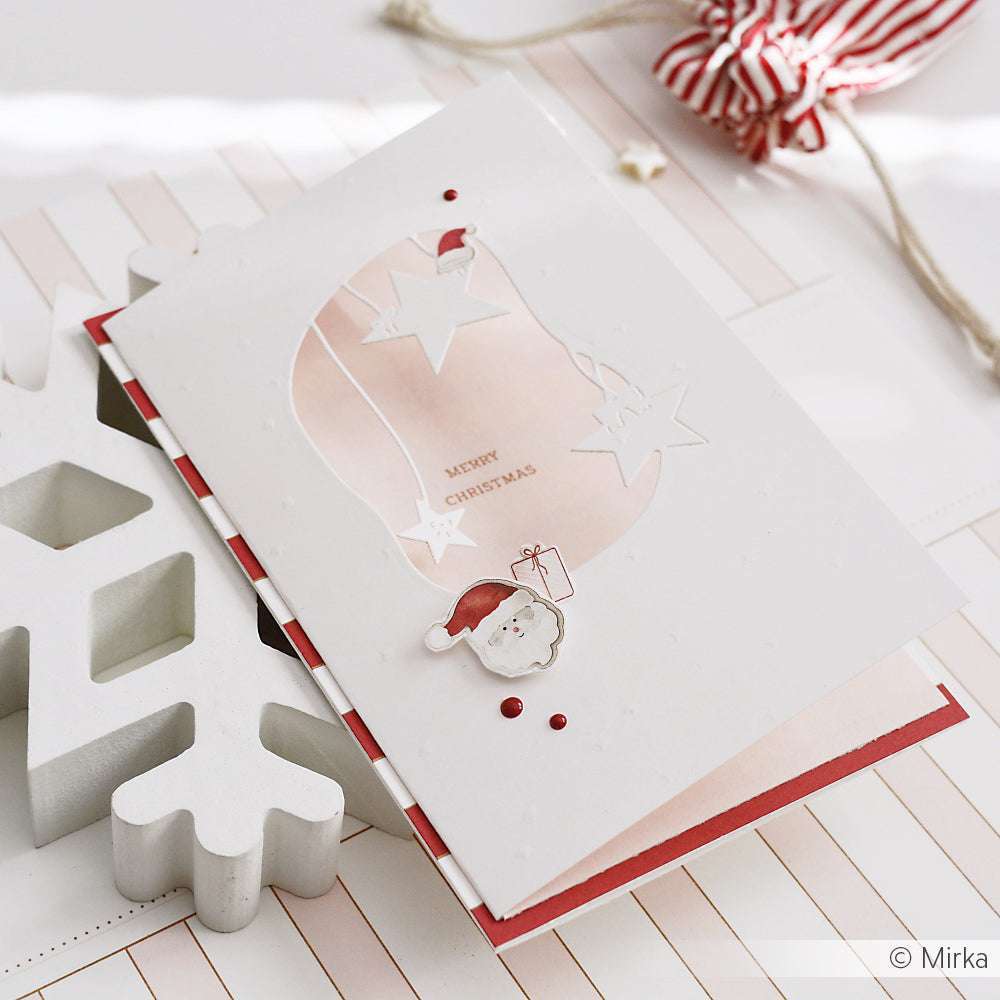 Handgefertigte Weihnachtskarte von Alexandra Renke aus Designpapier mit Weihnachtsmann und Sternen, die mit dem Sternen Mobile DieCut System erstellt wurden, sowie dem Text "Frohe Weihnachten", der neben einer weißen Schneeflockendekoration steht.