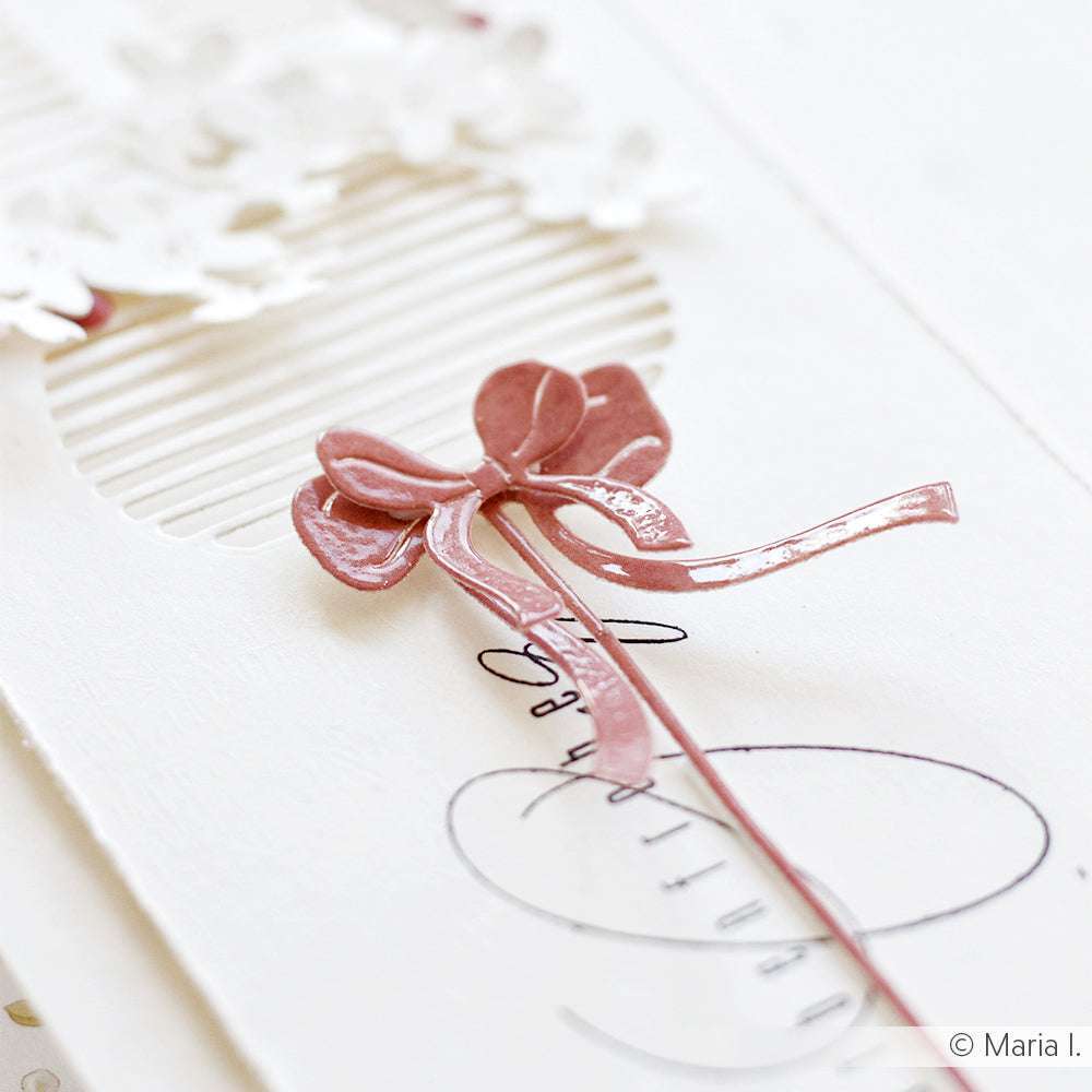 Nahaufnahme einer rosafarbenen Schleifenverzierung auf einer weißen, strukturierten, handgefertigten Geburtstagskarte mit floralen Details - hergestellt mit Alexandra Renke Motivstanze Schleifen am Stiel für präzise Schnitte und elegantes Design.