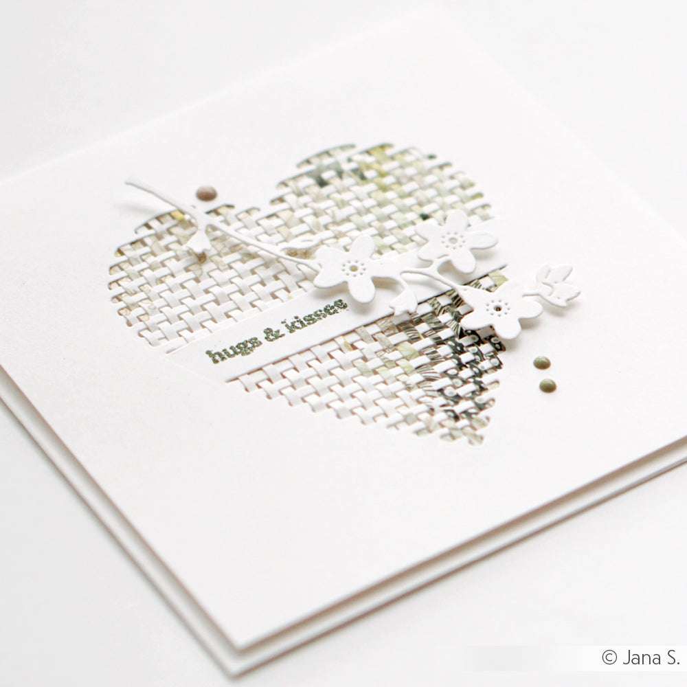 Weiße Karte mit einem herzförmigen Ausschnitt aus Alexandra Renke Deep Edge Motivstanzen, floralen Akzenten und "hugs & kisses" in grüner Schrift.