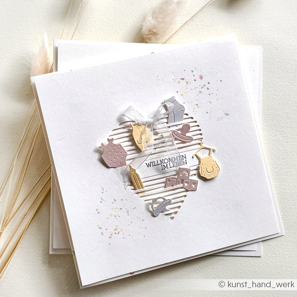 Weiße Grußkarte von Alexandra Renke mit Herzausschnitt, Anhängern zum Thema Baby und dem Text "Willkommen im Leben"; hergestellt mit PAPPcut®ies und Deep Edge Motivstanzen für einen eleganten Look.