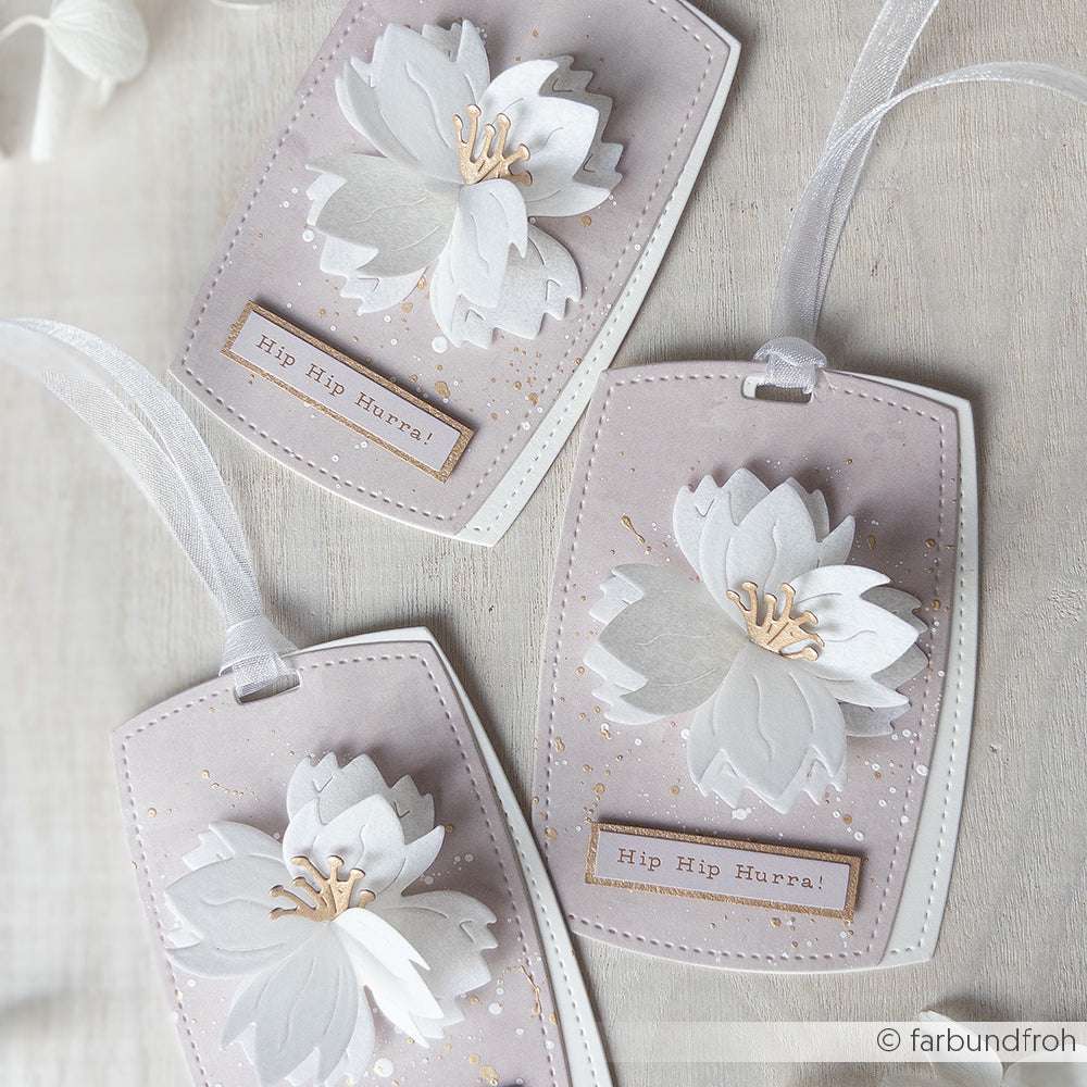 Drei dekorative Anhänger von Alexandra Renke mit PAPPcut®ies, weißen Papierblumen, "Hip Hip Hurra!"-Text und weißer Schleife auf hellem Hintergrund.