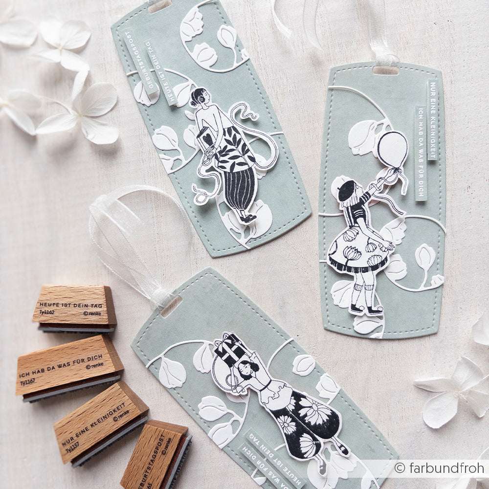 Drei pastellfarbene Lesezeichen mit Figuren im Vintage-Stil und weißen Blattmotiven, hergestellt mit der Alexandra Renke PAPPcut®ies Motivstanze Rechteck Etikett, sind umgeben von Stempeln und Papierblättern.