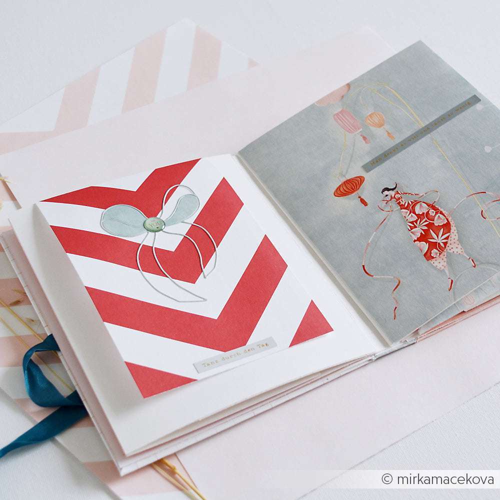 Offenes Scrapbook mit einer roten Chevron-Seite und einer illustrierten Frau mit Laternen, wunderschön verziert mit Alexandra Renke PAPPcut®ies und Deep-Edge-Stanzen.