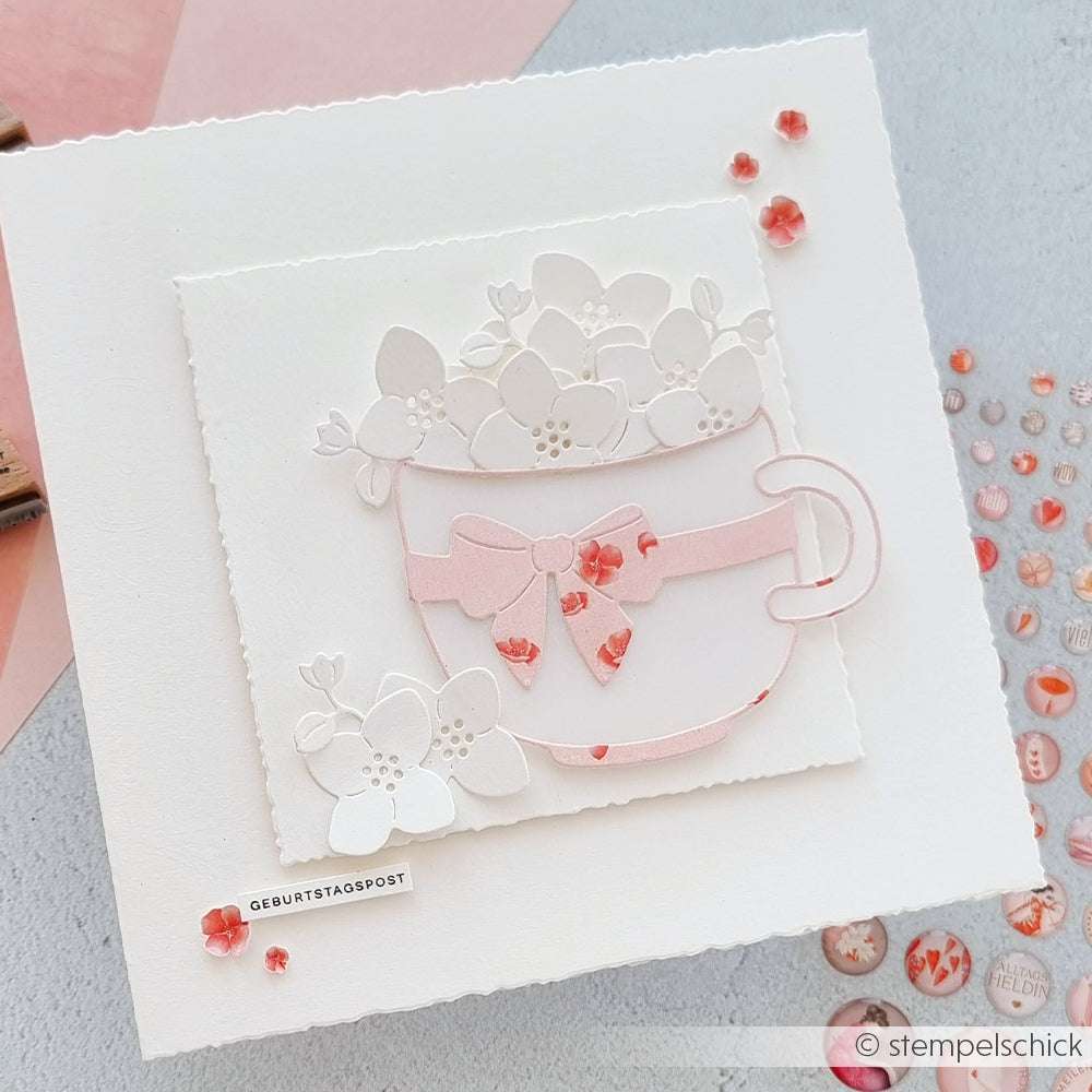 Handgemachte Geburtstagskarte von Alexandra Renke mit einer Teetasse aus der Motivstanze Große Schleifentasse, verziert mit weißen Blumen, einer rosa Schleife und Schmucksteinakzenten auf weißem Hintergrund.