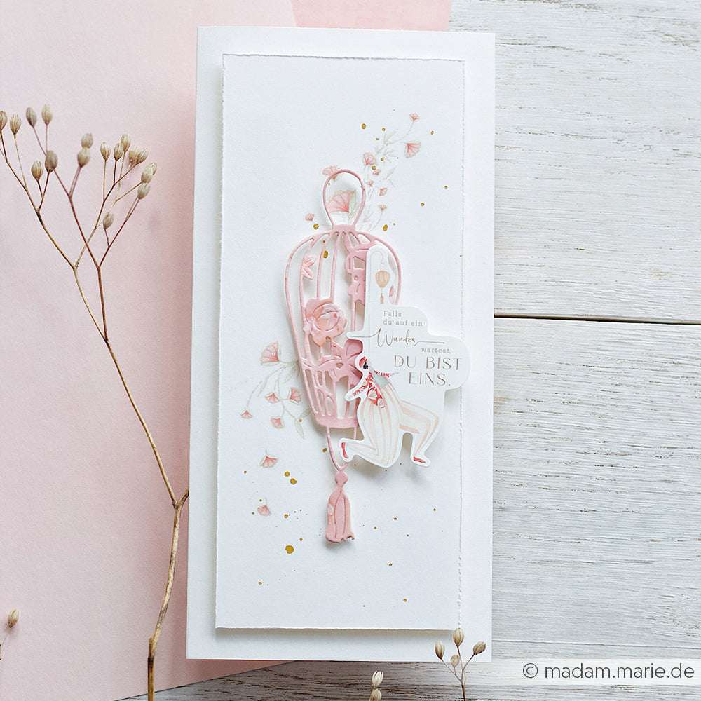 Handgefertigte Karte mit einem rosafarbenen Vogelkäfig, Blumen und deutschem Text, verziert mit getrockneten Blumen auf weißem Untergrund - hergestellt mit Alexandra Renke's Deep Edge Motivstanzen für komplizierte Details.
