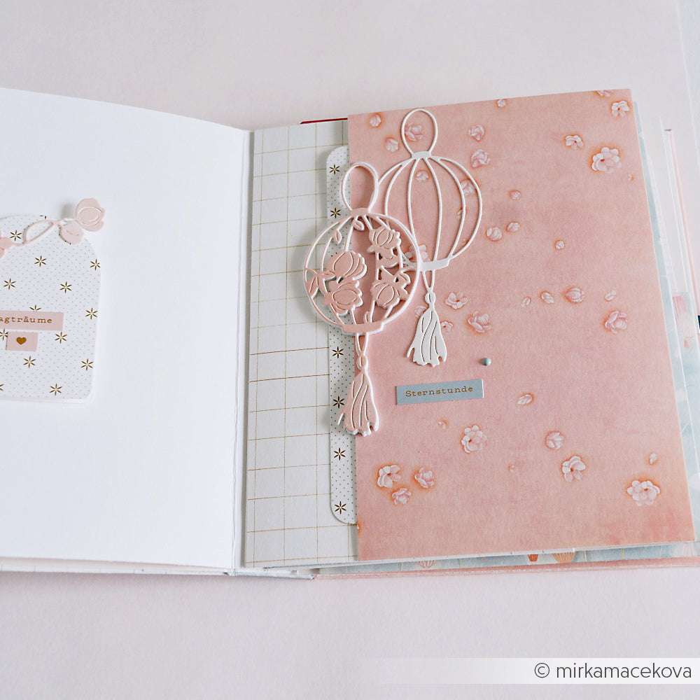 Geöffnetes Scrapbook mit rosafarbener Blumenseite und weißen Ballonausschnitten, die mit der Stanze Großer runder Lampion von Alexandra Renke hergestellt wurden, sowie gemustertem Papier - perfekt für kreative Projekte mit PAPPcut®ies.