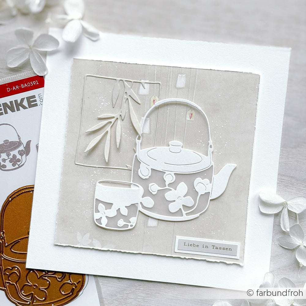 Eine bezaubernde Karte mit einer weißen Teekanne und einer Teetasse mit Blumenmotiven auf beigem Hintergrund, gestaltet mit dem Motivstanze Großes Teeset von Alexandra Renke.