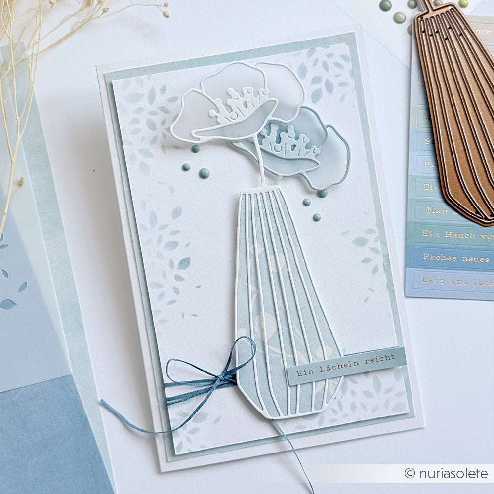 Handgefertigte Alexandra Renke Karte mit zwei hellen Blumen in einer großen Blumenvase, blauer Schleife und dem Text "Ein Lächeln reicht" - hergestellt mit PAPPcut®ies für eine präzise Verarbeitung.