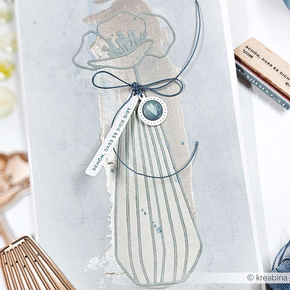 Handgemachte Karte von Alexandra Renke mit einer mit Deep Edge Motivstanzen geprägten Vase von PAPPcuties, einer blauen Schleife und einem Anhänger mit der Aufschrift "Schön, dass es dich gibt.