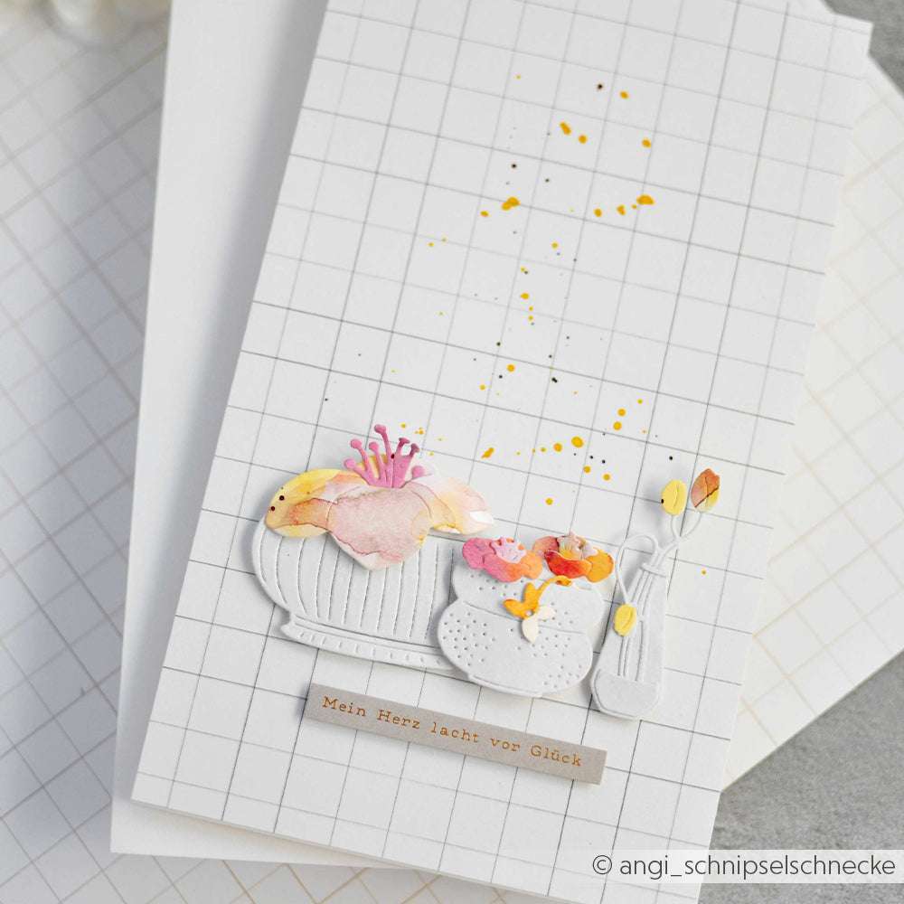 Handgefertigte Karte von Alexandra Renke mit aquarellierten Blumen in Vasen auf einem Gitterhintergrund, hervorgehoben durch ein deutsches Textetikett und zarte Details mit der Motivstanze Blumentopf für zusätzlichen Charme.