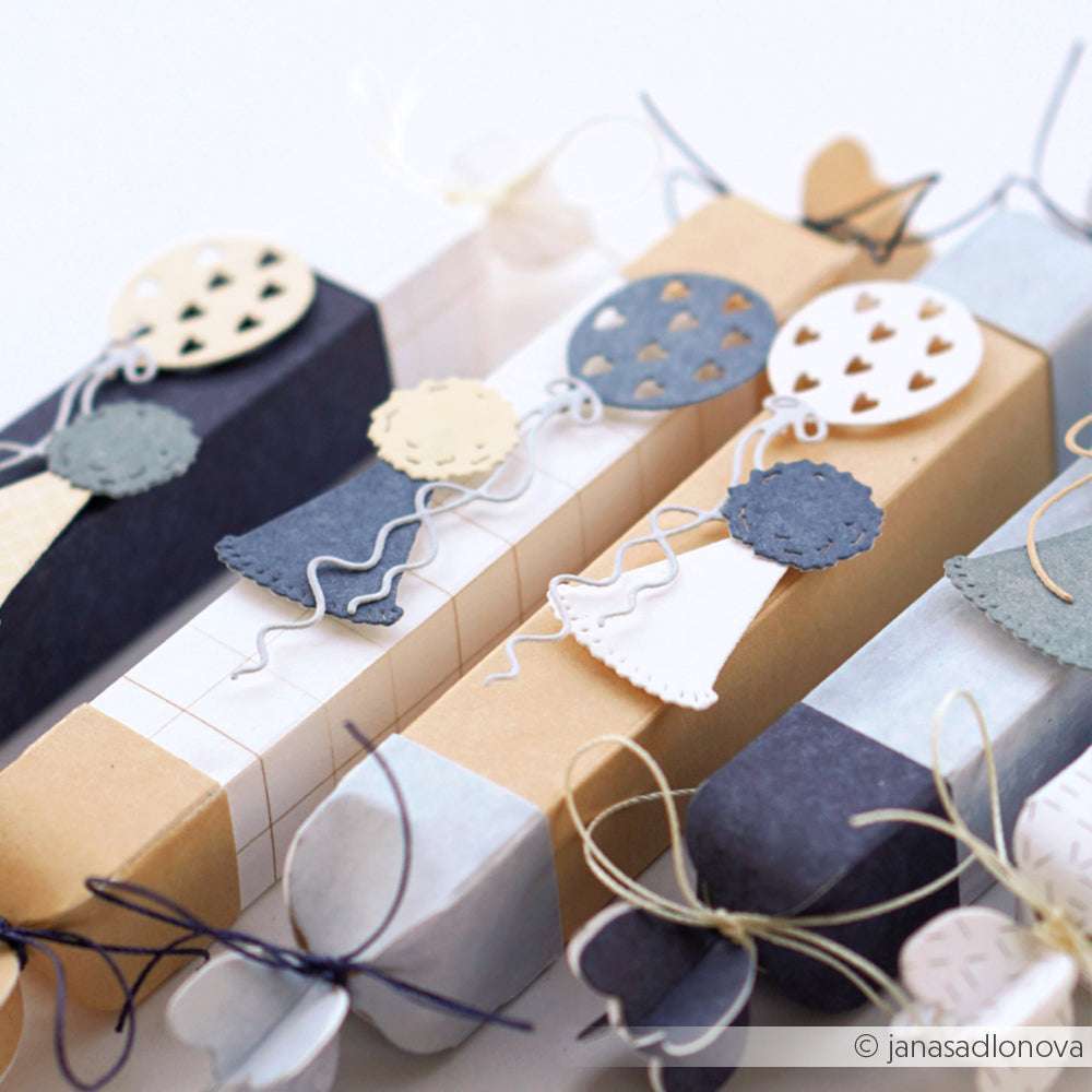 Handgefertigte Geschenkboxen von Alexandra Renke, verziert mit Papierballons, Herzen und PAPPcuties-Akzenten in neutralen und blauen Tönen, verziert mit Schleifen.