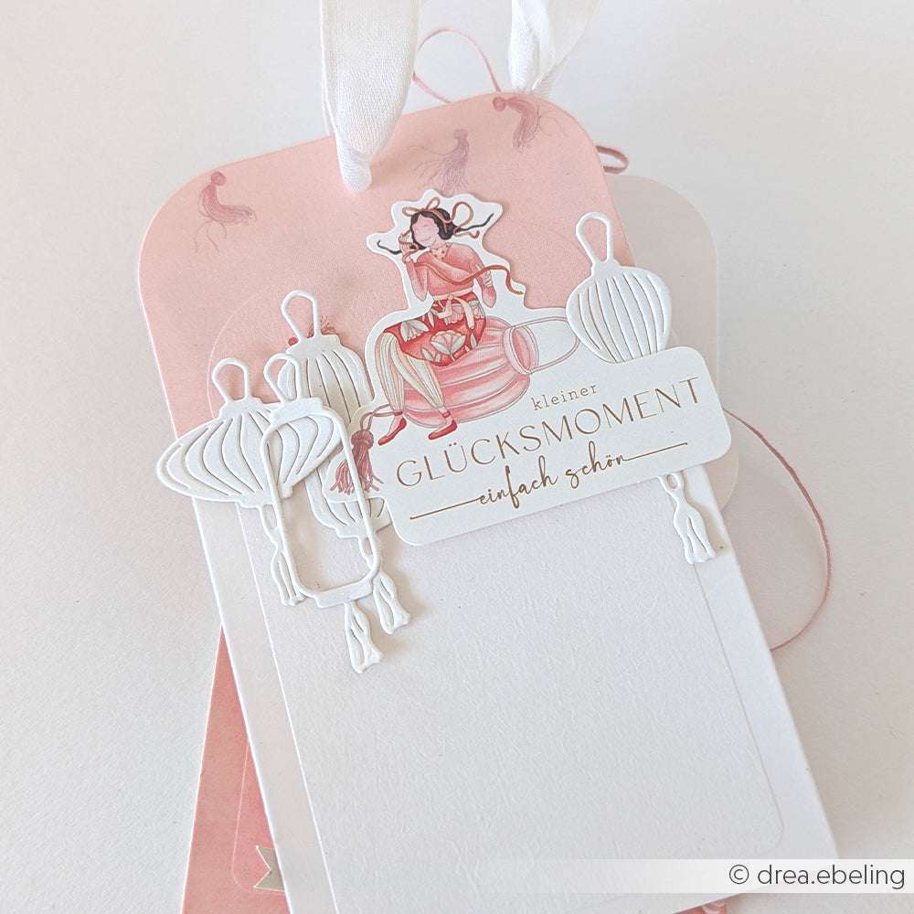 Weißer und rosafarbener dekorativer Geschenkanhänger von Alexandra Renke mit einer Mädchenillustration, die mit PAPPcut®ies und Deep Edge Motivstanzen hergestellt wurde, sowie dem Text "kleiner Glücksmoment - einfach schön".