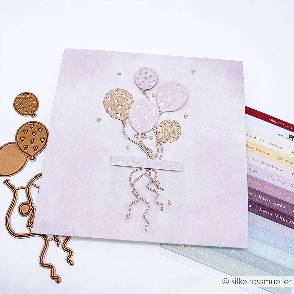Eine handgefertigte Karte von Alexandra Renke mit goldenen und rosafarbenen Ballonausschnitten, hergestellt mit Motivstanze Luftballons und PAPPcut®ies, sowie deutschem Text auf hellem Hintergrund.