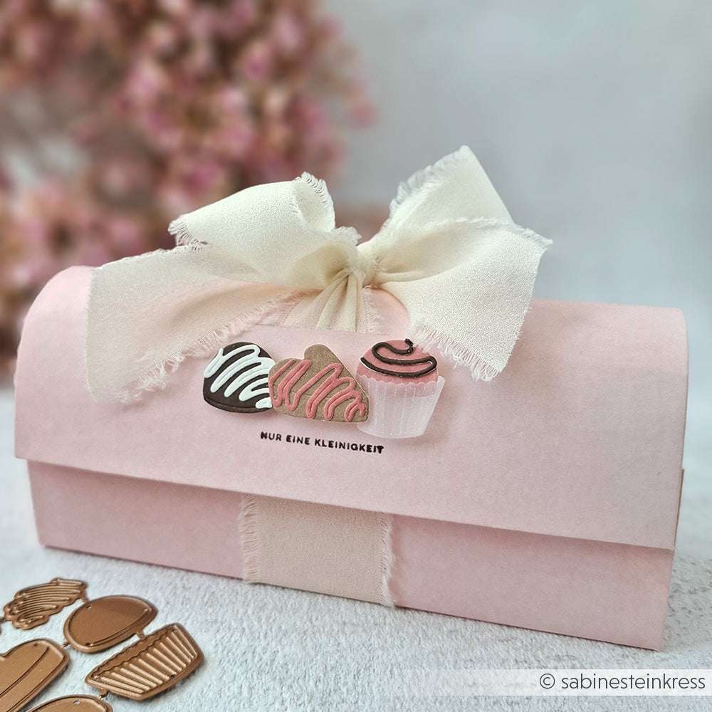 Rosa Geschenkbox mit cremefarbener Stoffschleife, verziert mit Schokoladen- und Cupcake-Zeichnungen auf der Vorderseite, hergestellt mit der Motivstanze Pralinenset von Alexandra Renke.