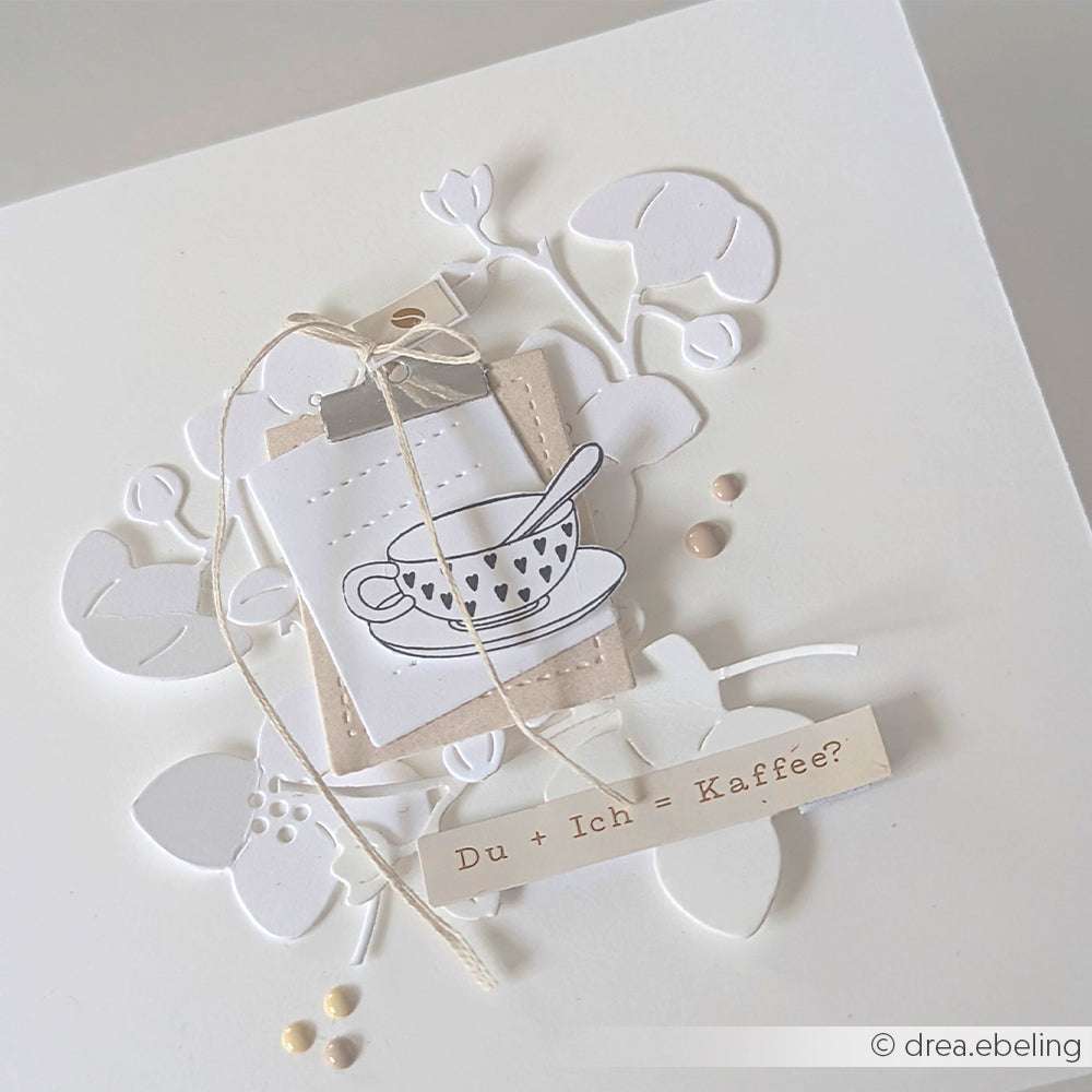 Eine handgefertigte Karte von Alexandra Renke zeigt eine Teetasse, ein Blumenmuster und "Du + Ich = Kaffee?" auf einem Papierstreifen, der mit PAPPcut®ies hergestellt und mit Deep Edge Motivstanzen verziert wurde.