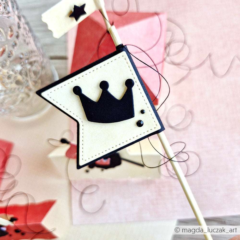 Eine cremefarbene Fahne von Alexandra Renke mit schwarzer Krone und Punktmuster, die mit der Motivstanze große Fahne gestaltet wurde, ist auf einem Stock vor rosa Hintergrund angebracht.