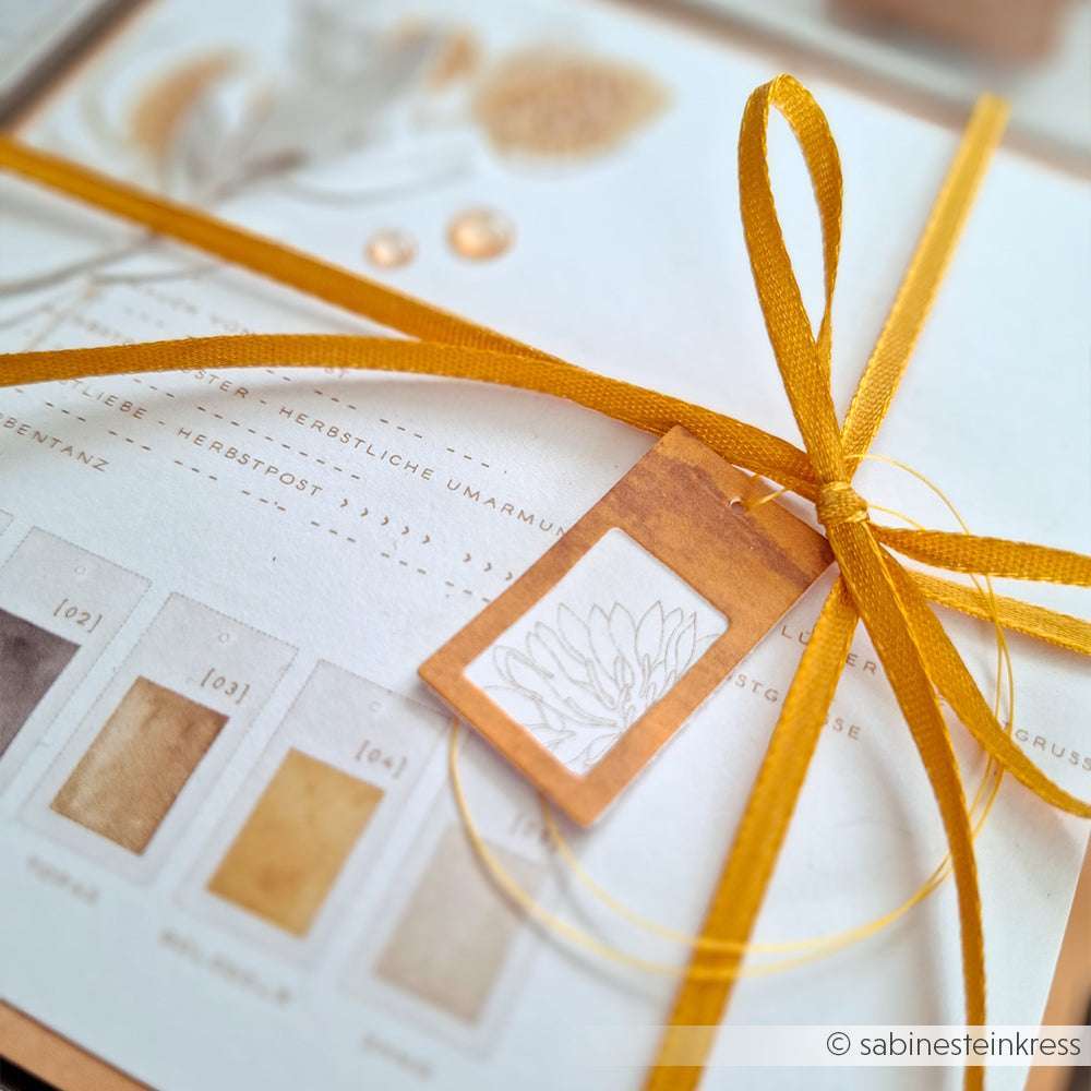 Nahaufnahme einer Karte mit herbstlichen Farbtönen, gebunden mit einem gelben Band und einem kleinen Blumenanhänger, hergestellt mit Alexandra Renke Deep Edge Motivstanzen für komplizierte Details.