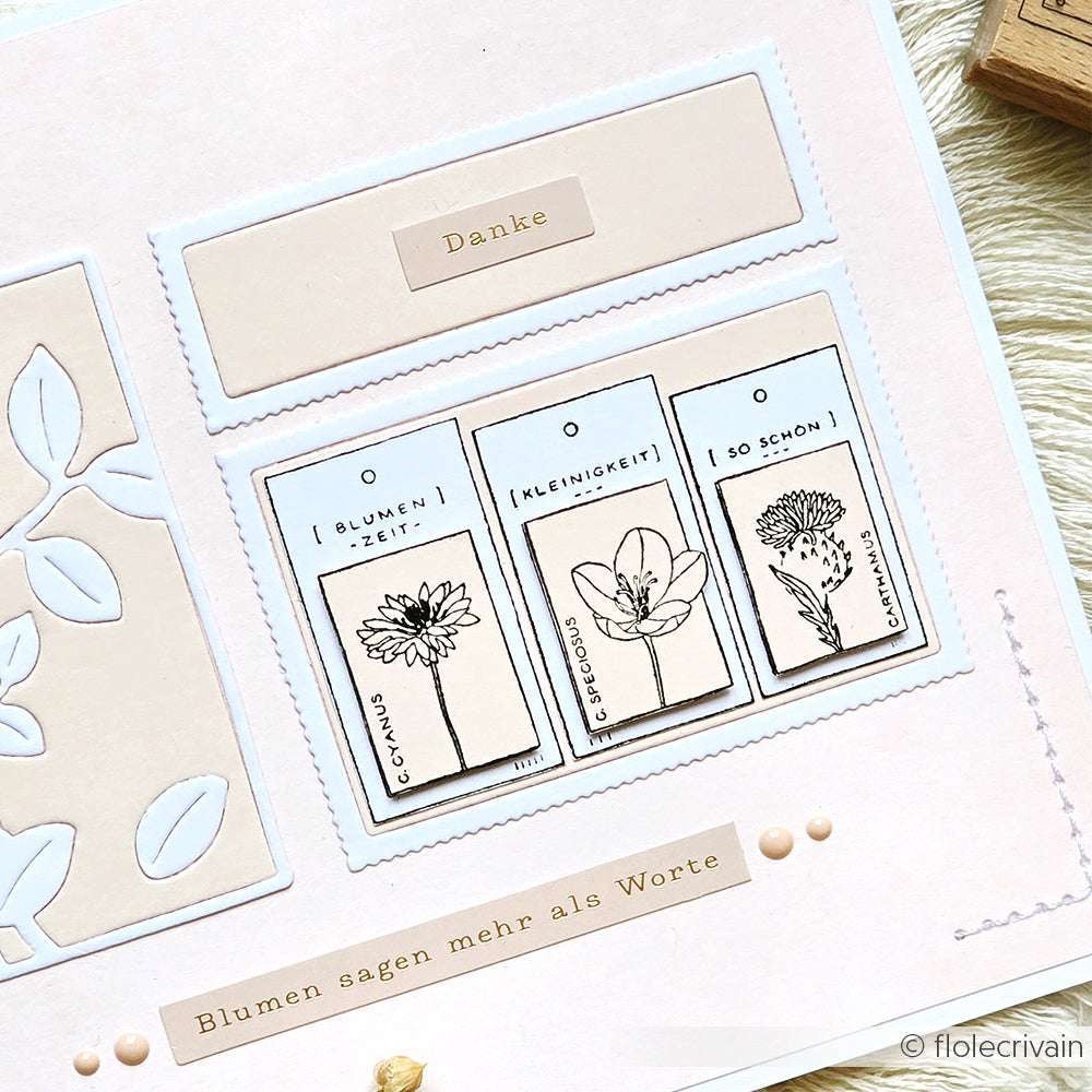 Eine handgefertigte Karte von Alexandra Renke mit Blumenillustrationen, deutschem Text und beigen und weißen dekorativen Papierelementen, die mit Deep Edge Motivstanzen für elegante Details verarbeitet wurden.