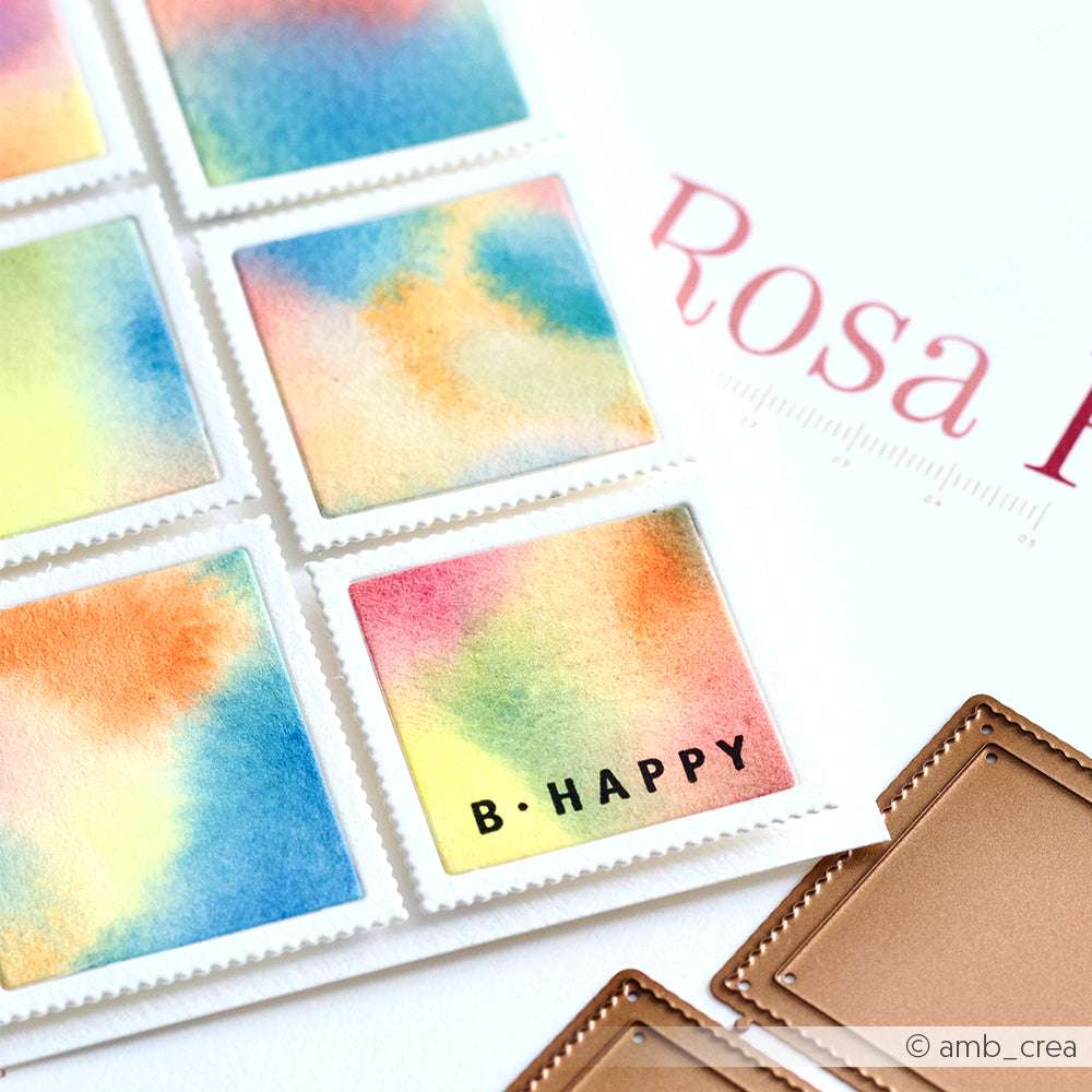 Bunte Aquarellstempel, darunter einer mit dem Text B-HAPPY, werden neben einem Teil des Alexandra Renke-Etiketts und den Deep Edge Motivstanzen aus Metall gezeigt.