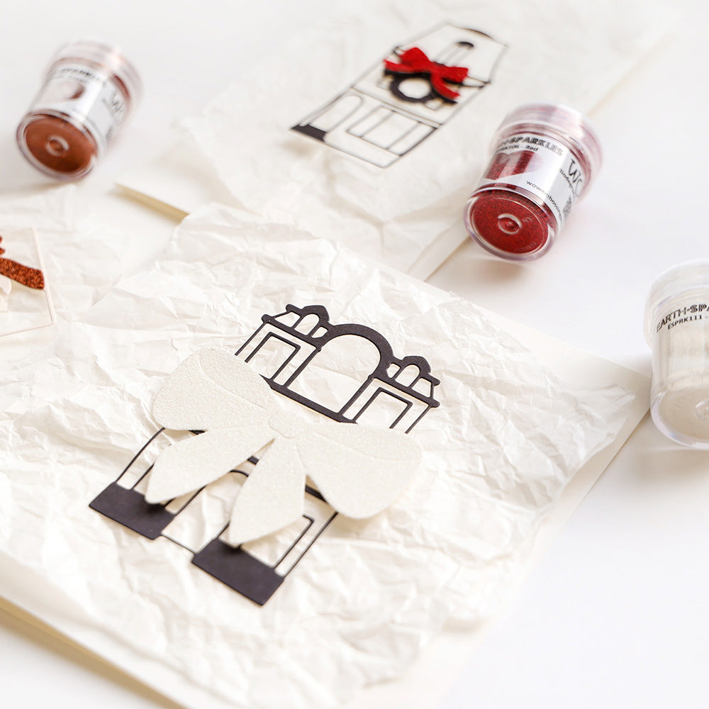 Zerknüllte Papiere mit schwarzen Bauskizzen aus Alexandra Renke Motivstanze Edles großes Haus, große weiße und rote Schleifen und Glitzertöpfchen auf weißem Untergrund.