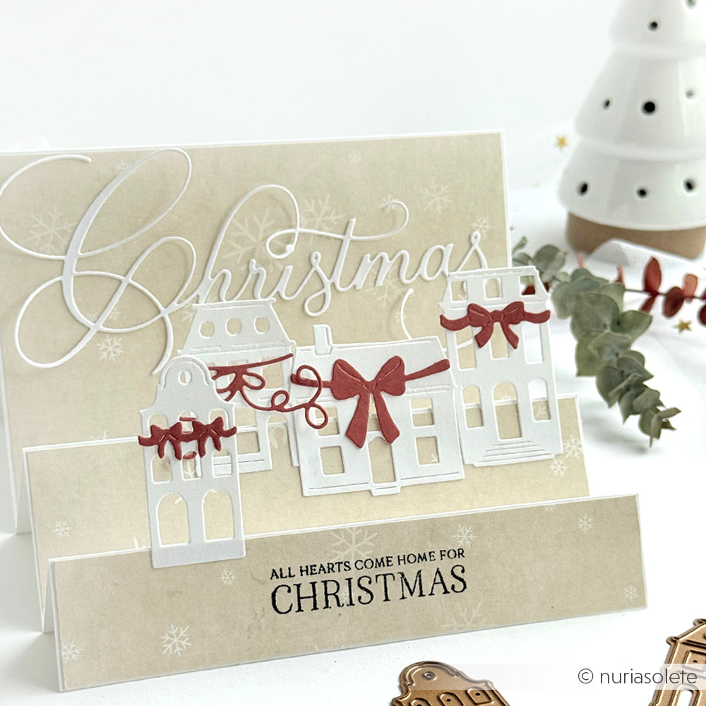 Handgemachte Weihnachtskarte von Alexandra Renke mit weißen Häusern, die mit DieCut Systemen hergestellt wurden, roten Schleifen und festlichem Text auf beigem Hintergrund.