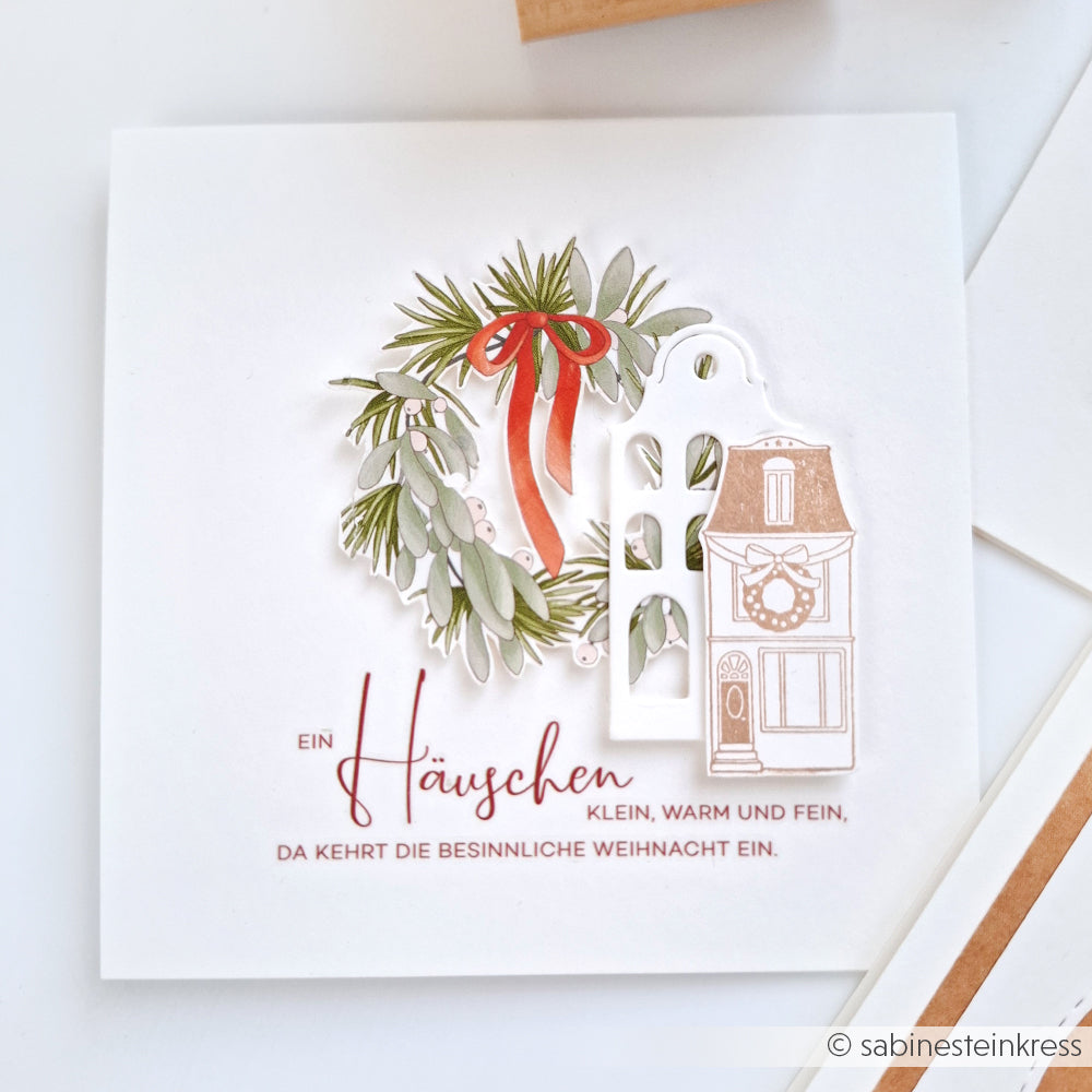 Diese Weihnachtskarte von Alexandra Renke zeigt ein Haus, einen Kranz mit roter Schleife und einen deutschen Weihnachtstext auf weißem Grund - ideal für Fans von Motivstanze und Designpapieren.