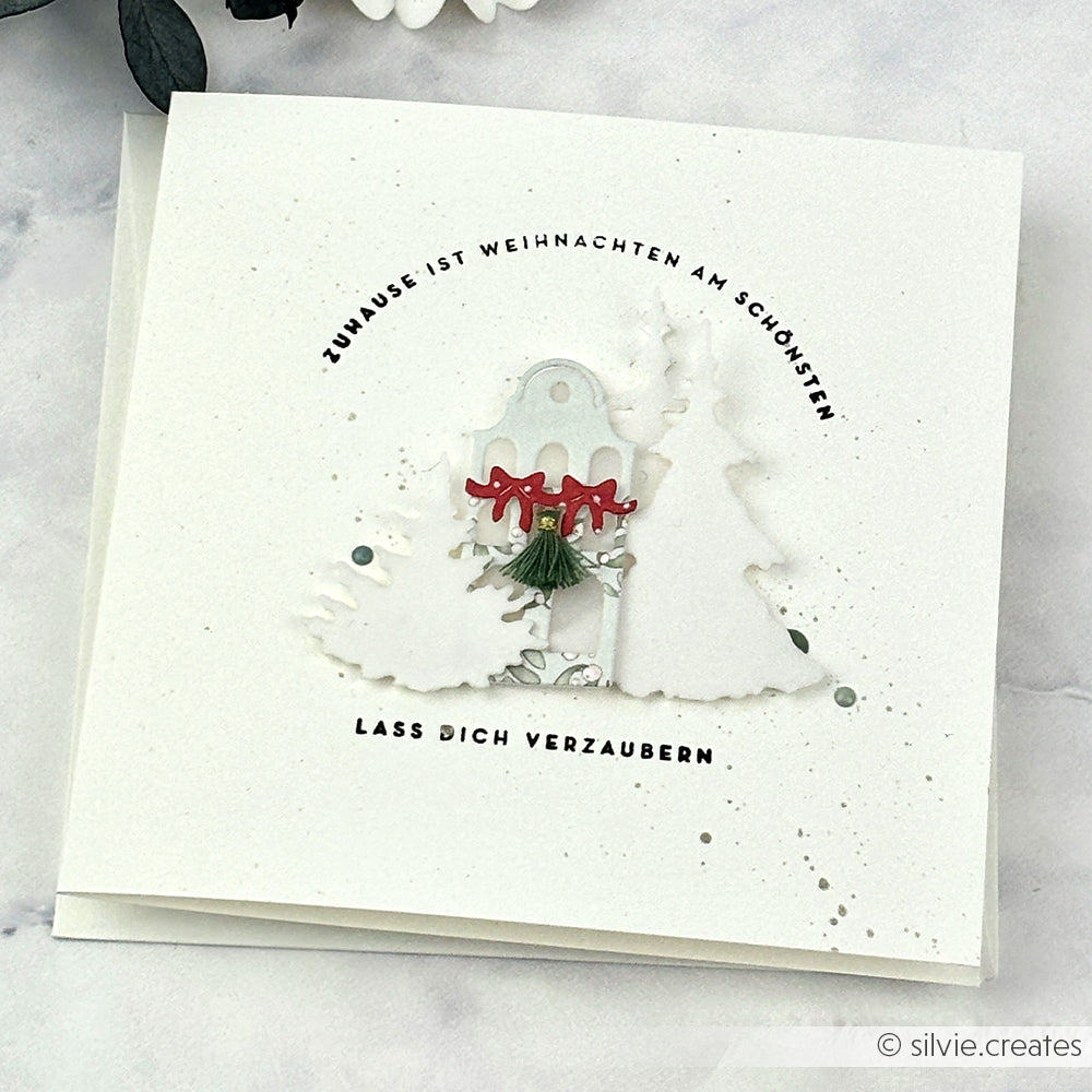 Weiße Weihnachtskarte mit geschichteten weißen Bäumen, roten Schleifen und deutschem Text in einem kreisförmigen Design, hergestellt mit Alexandra Renke Designpapieren und der Motivstanze Feines Schleifenhaus für elegante Details.