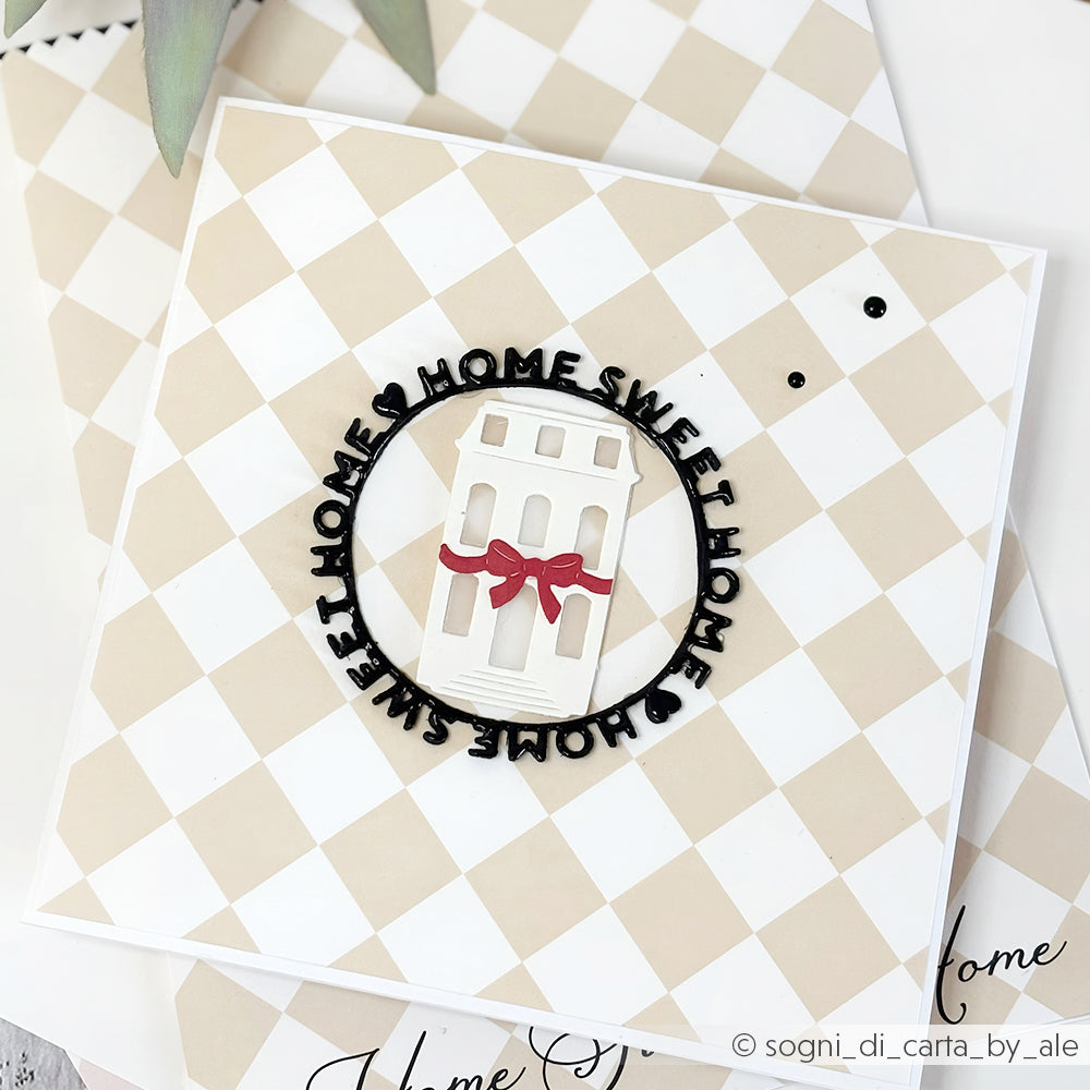 Quadratische Karte mit beige-kariertem Hintergrund, weißem Haus aus der Alexandra Renke Motivstanze Schleifenhaus, roter Schleife und "Home Sweet Home" in schwarzer Rundschrift - eine charmante Ergänzung Ihrer Designpapiere und Stanzsysteme.