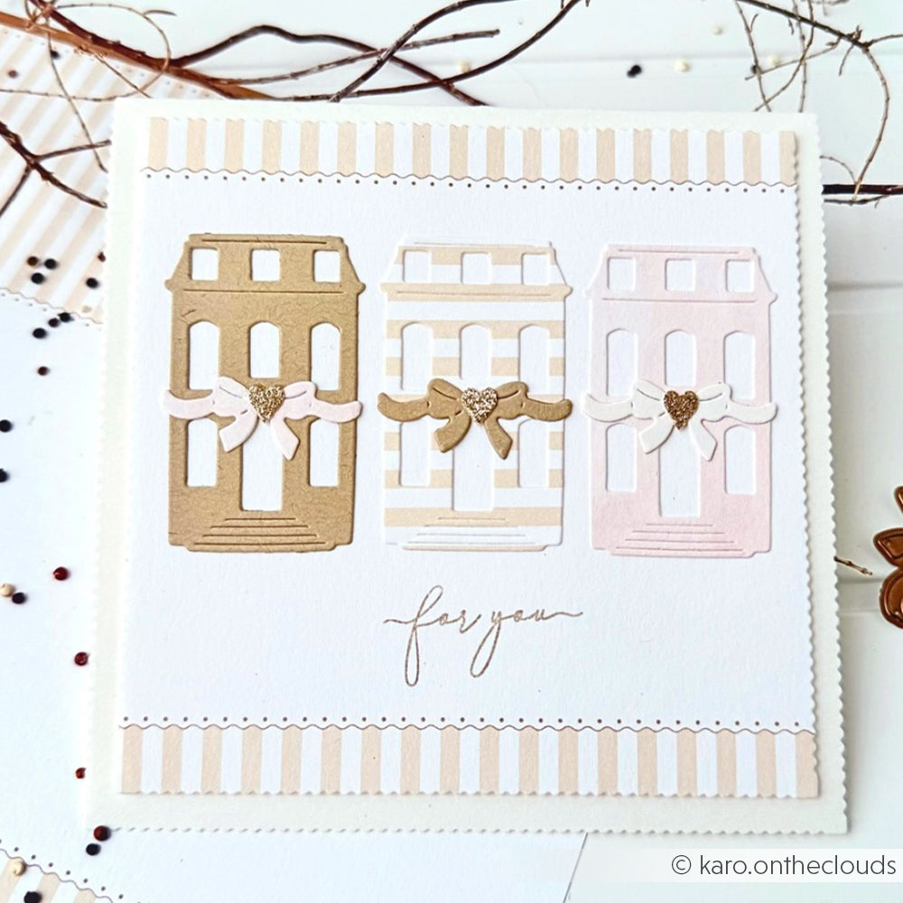 Eine handgefertigte Karte von Alexandra Renke mit drei pastellfarbenen Stadthäusern, Schleifenband und dem Schriftzug "for you" darunter. Hergestellt aus Designpapieren mit aufwendigen Motivstanze-Details für eine charmante, einzigartige Note.
