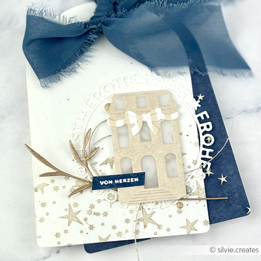 Handgefertigter Weihnachtsanhänger von Alexandra Renke mit Haus, Sternen, blauer Schleife und "VON HERZEN"-Schriftzug. Gefertigt mit Designpapieren und DieCut Systemen für einzigartige Details.