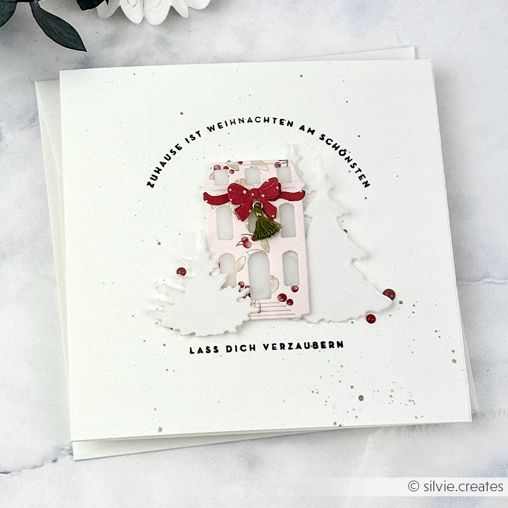 Alexandra Renke handgefertigte Weihnachtskarte mit einem geschmückten Haus und Bäumen mit deutschem Text in einem kreisförmigen Layout, hergestellt mit hochwertigen Designpapieren und einer Motivstanze für komplizierte Details.