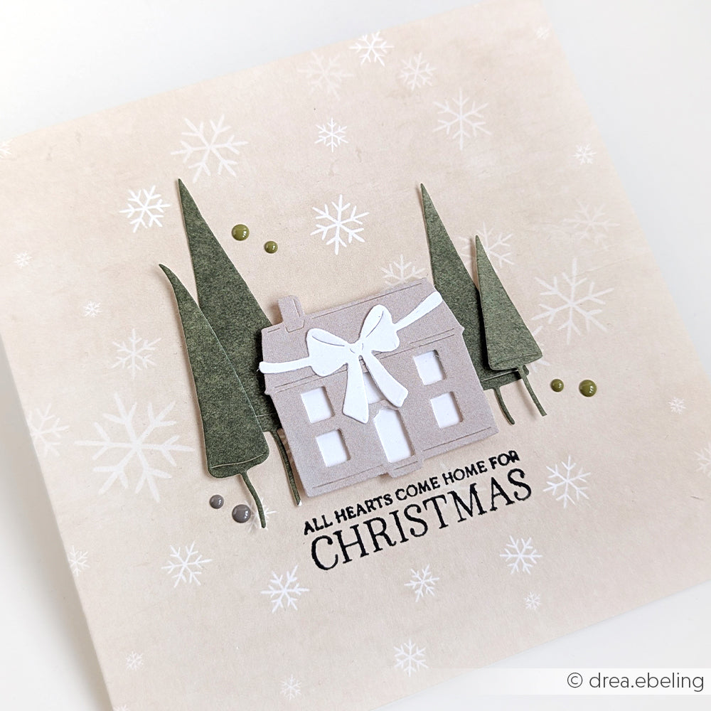 Eine Weihnachtskarte von Alexandra Renke mit einem Haus, Bäumen, Schneeflocken, die mit DieCut Systemen hergestellt wurden, und der Botschaft "All hearts come home for Christmas".