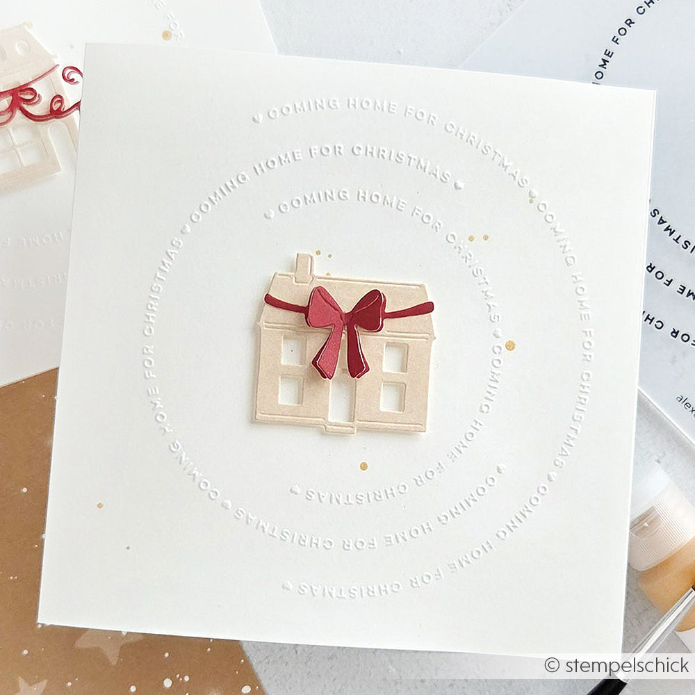 Die minimalistische Karte von Alexandra Renke, die mit Designpapieren gestaltet wurde, zeigt ein kleines Haus und eine rote Schleife, umgeben von dem geprägten Text "Coming Home for Christmas".