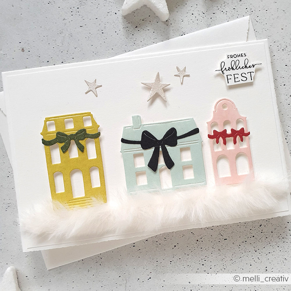Handgemachte Weihnachtskarte von Alexandra Renke mit pastellfarbenen Häusern, Schleifen, Sternen und Kunstschnee mit Motivstanze und festlichen Designpapieren. Auf der Vorderseite steht "Frohes Fest.