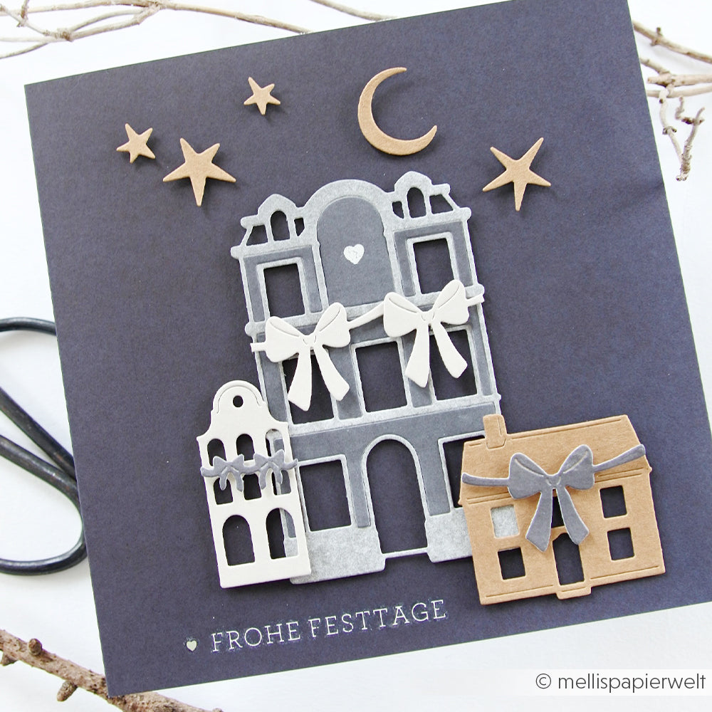 Handgefertigte Weihnachtskarte von Alexandra Renke aus Designpapier mit Papierhäusern, Sternen und einem Mond auf dunklem Hintergrund. Der Schriftzug "FROHE FESTTAGE" auf der Vorderseite sorgt für eine festliche Note.