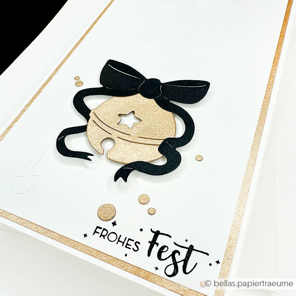 Handgefertigte Karte mit einer goldenen Glocke, die mit der Alexandra Renke Motivstanze Fröhliche Sternenglocke ausgeschnitten wurde, schwarzer Schleife, Text "Frohes Fest" auf weißem Designpapier und einem goldenen Rand.