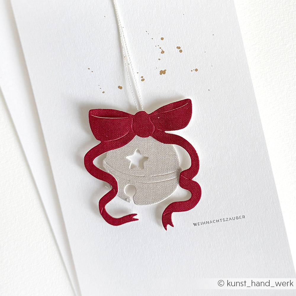 Grußkarte von Alexandra Renke mit silbernem Glockenornament und roter Schleife, mit dem Schriftzug "WEIHNACHTSZAUBER". Hergestellt mit Dies und Designpapieren für einen festlichen, handgefertigten Look.