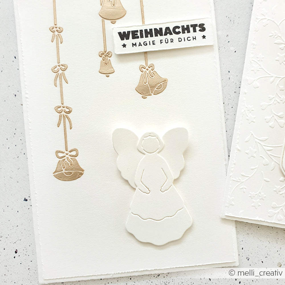 Handgefertigte Weihnachtskarte von Alexandra Renke aus hochwertigem Designpapier mit einem eleganten Engelsausschnitt, goldgeprägten Glocken und einem festlichen WEIHNACHTS"-Grußetikett.