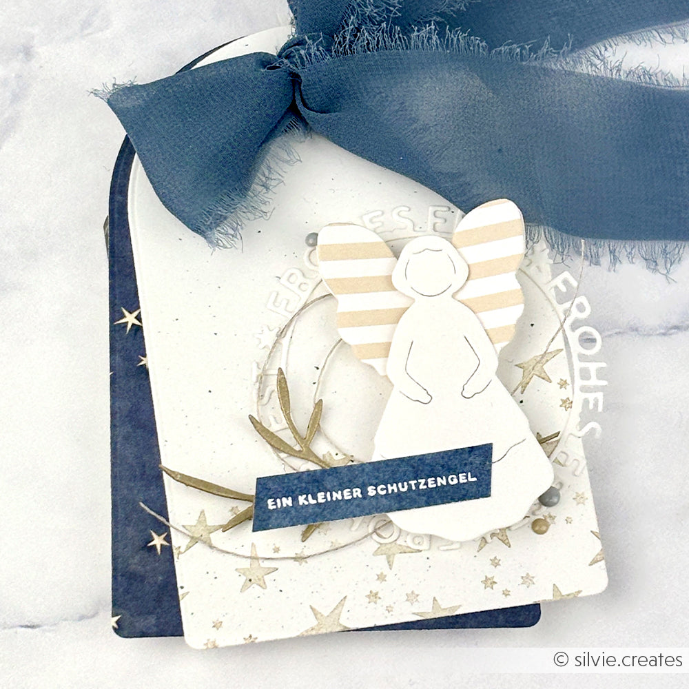 Handgefertigter Geschenkanhänger von Alexandra Renke mit einer Motivstanze Anmutiger Engel, blauem Band, deutschem Text auf geschichtetem Designpapier und Sternakzenten.