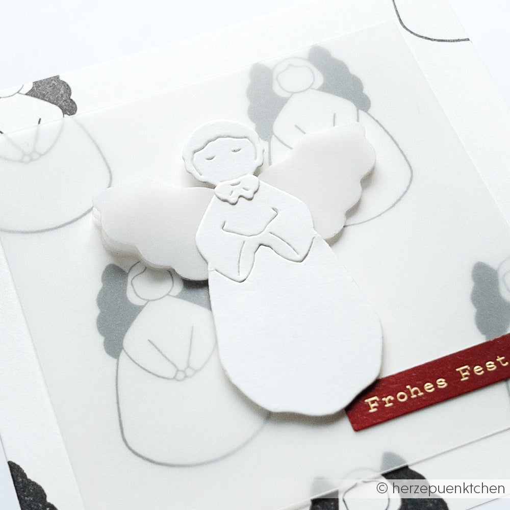 Eine Engelskarte aus weißem Papier mit skizzierten Engeln, gestaltet mit Alexandra Renke Designpapieren und der Motivstanze Sanfter Engel DieCut Systeme, veredelt mit einem roten Weihnachtsgruß-Etikett "Frohes Fest".