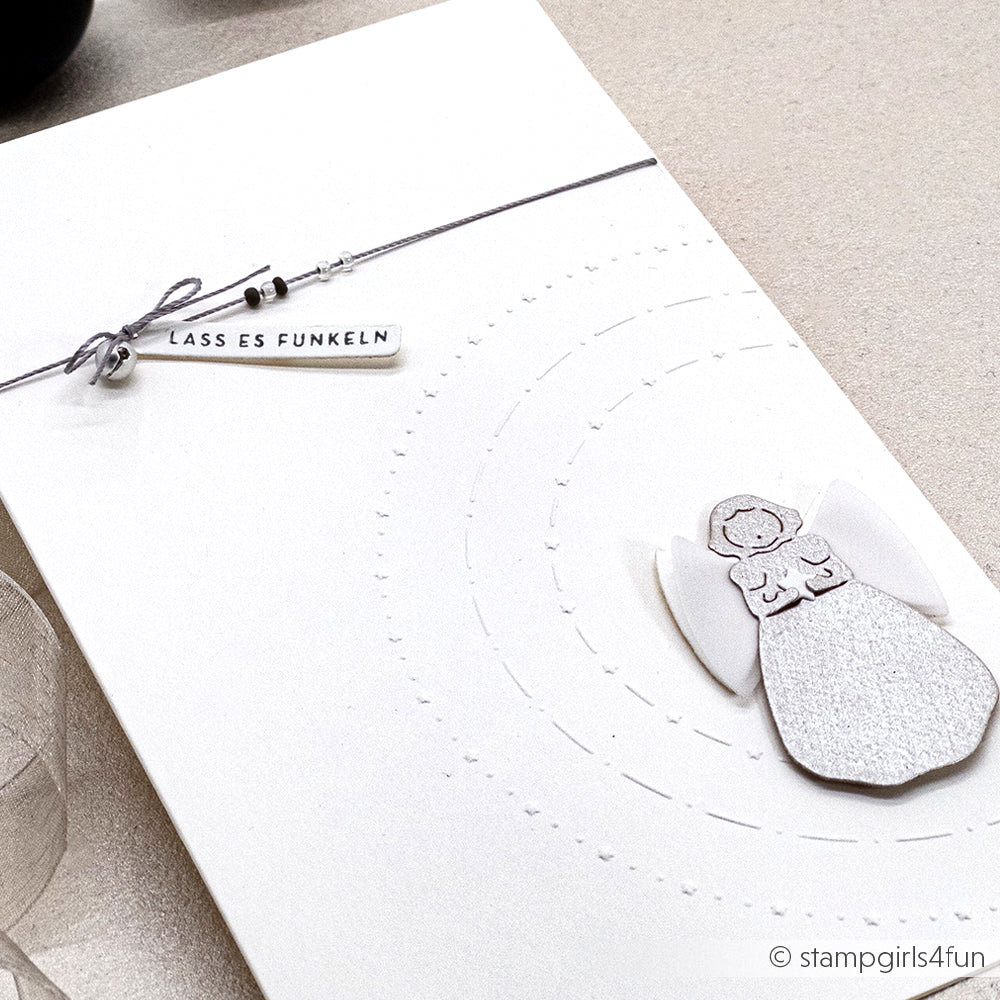 Weiße Karte von Alexandra Renke aus feinem Designerpapier, mit einer Singender Engel-Stanzung und einem "LASS ES FUNKELN"-Anhänger an einer Schnur oben links.