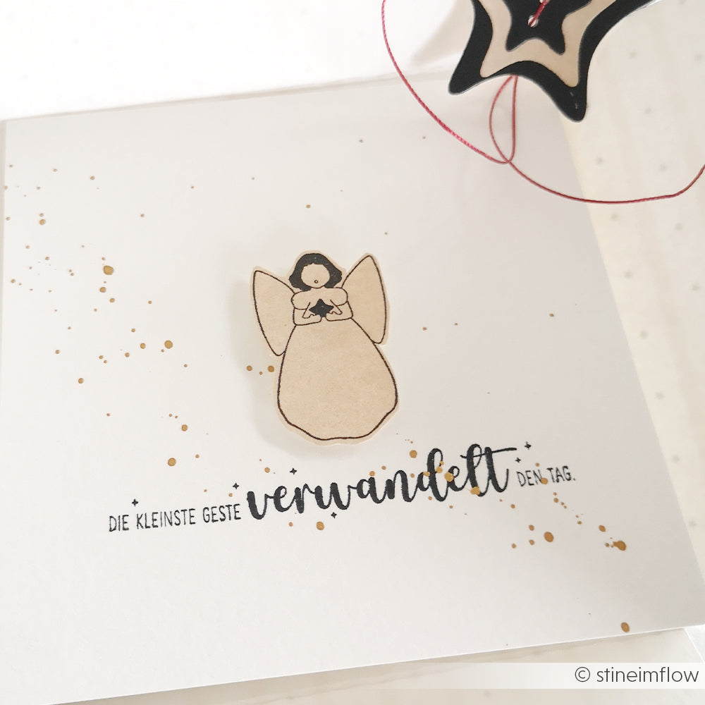 Eine handgefertigte Engelskarte von Alexandra Renke mit deutschem Text und Goldspritzern, teilweise verdeckt durch ein schwarzes Sternenornament, hergestellt mit der Motivstanze Singender Engel für eine elegante Note.