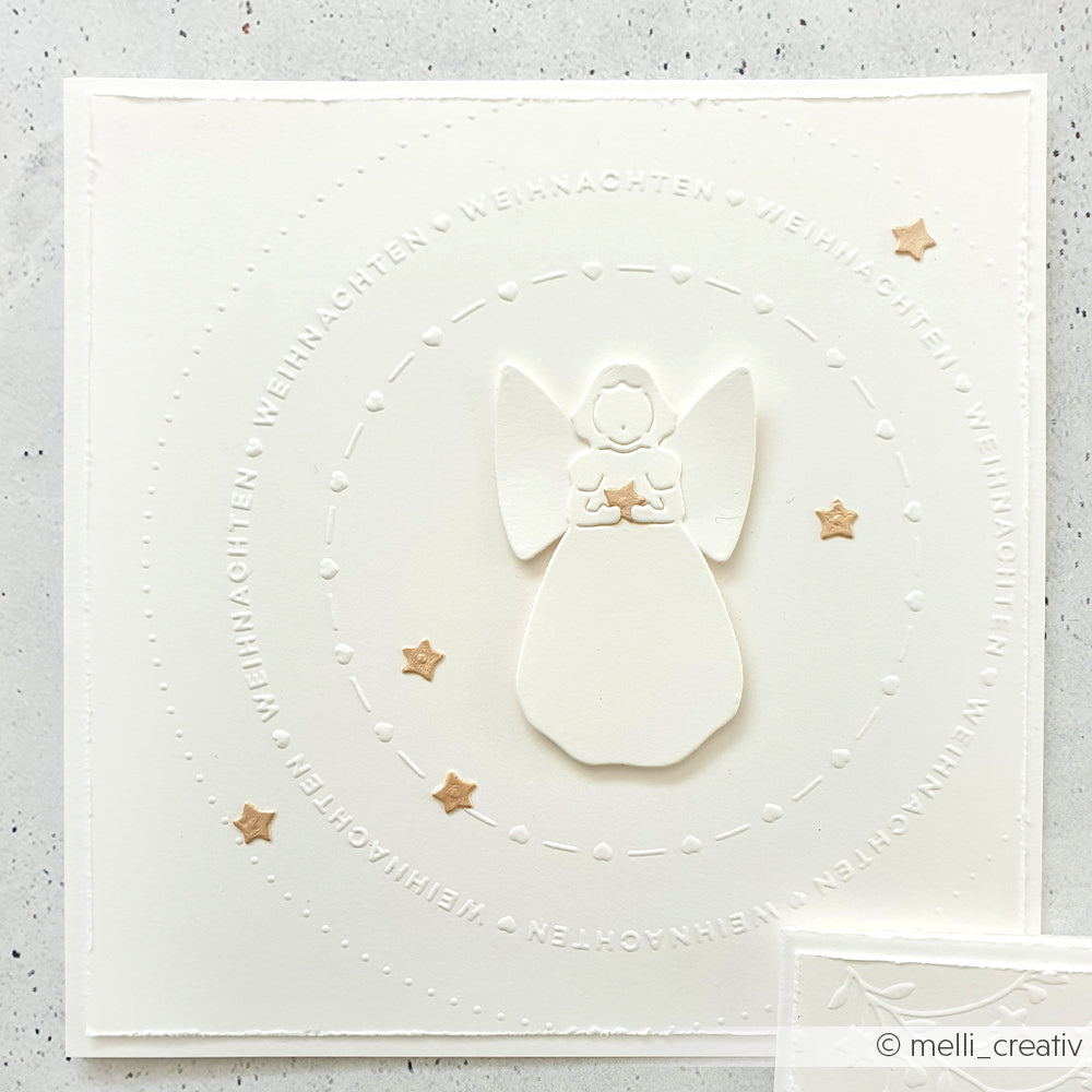 Weiße Karte von Alexandra Renke mit einem erhabenen Engel aus der Motivstanze Singender Engel, umgeben von goldenen Sternen und dem kreisförmig wiederholten "WEIHNACHTEN".