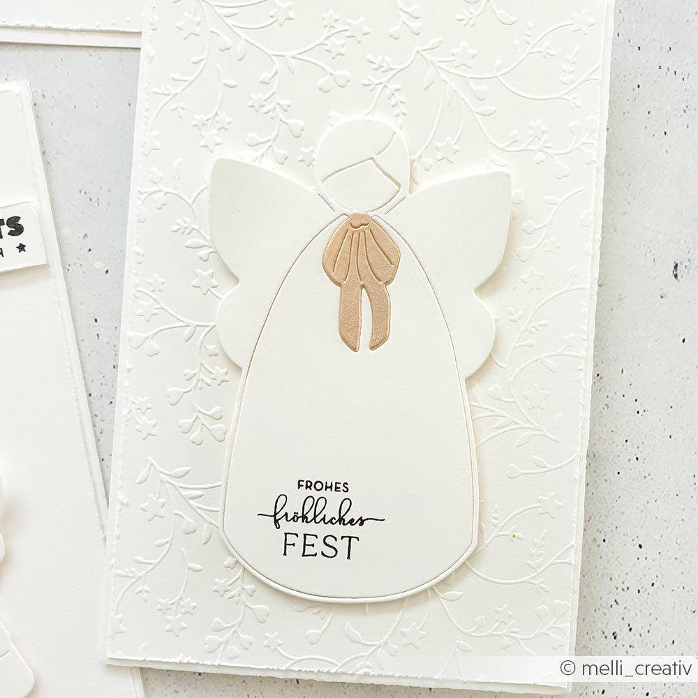Weißer Papierengel, hergestellt mit Alexandra Renke Designpapiere und Motivstanze Großer Engel, mit geprägtem Blumenhintergrund und dem Spruch "Frohes, glückliches Fest" auf dem Kleid.