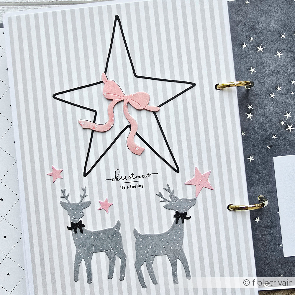 Zwei graue Rentiere und rosa Sterne unter einem großen Sternumriss von Alexandra Renke, mit einer rosa Schleife auf gestreiftem Designpapier mit der Aufschrift "Weihnachten".